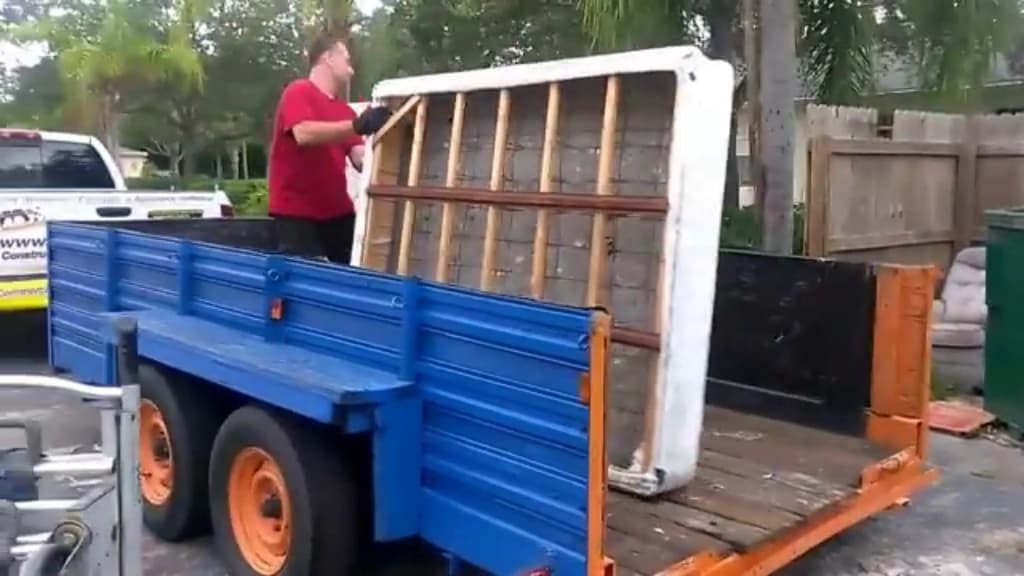 Hauler lifting a large cabinet onto a flatbed trailer parked beside the property