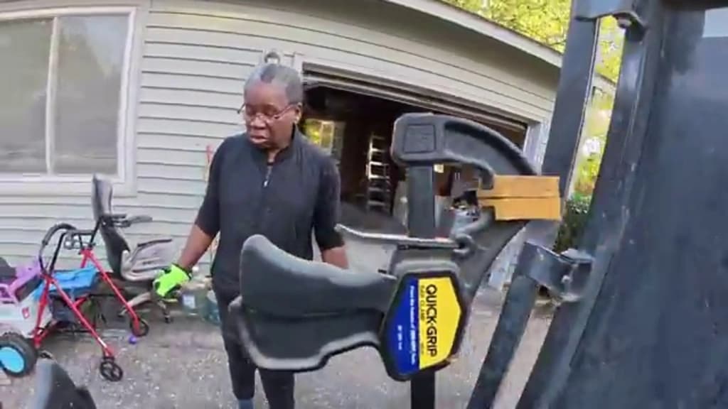 Homeowner carrying a chair out to the trailer during a downsizing cleanout, with a walker and mobility equipment beside the garage