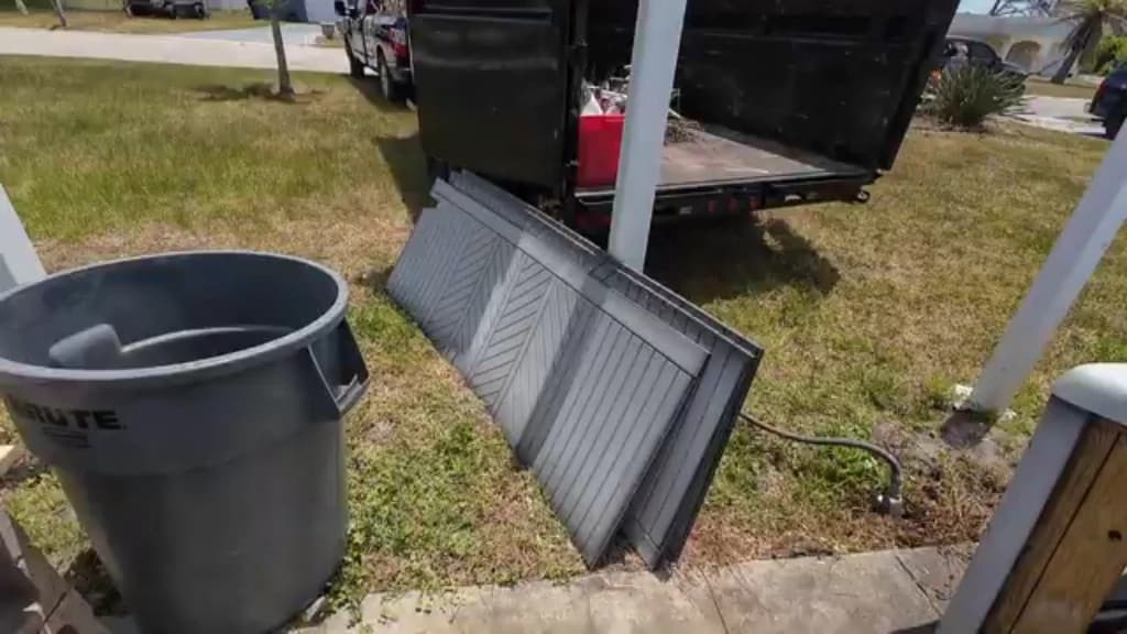 Trash can and a metal panel staged on a lawn beside a loaded dump truck