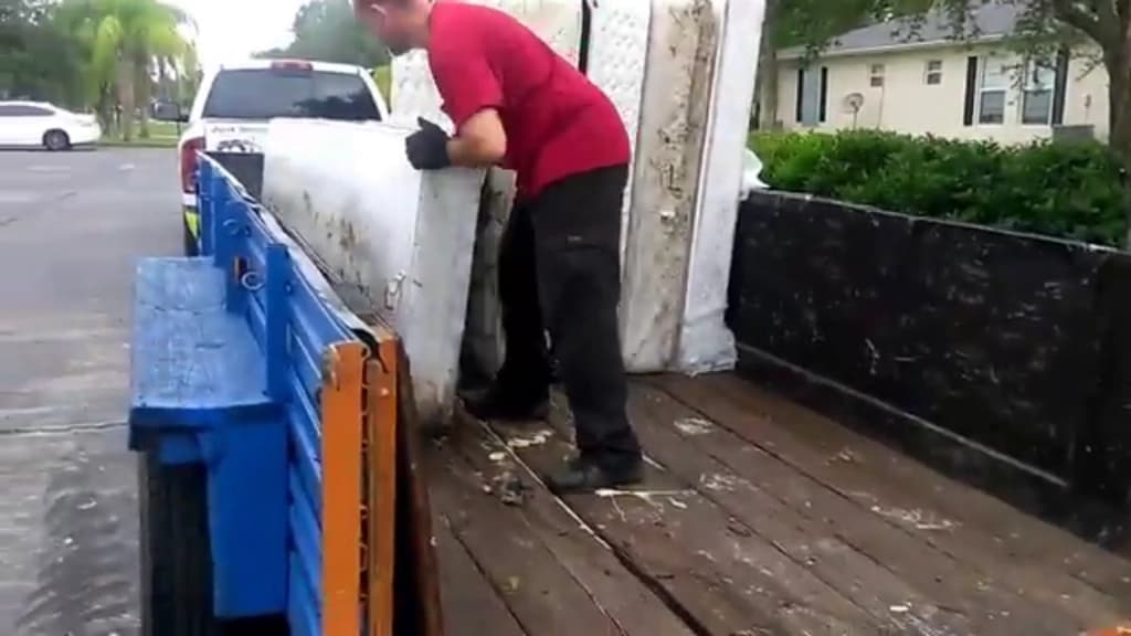 Crew member loading a mattress onto a trailer at the curb outside a residential property