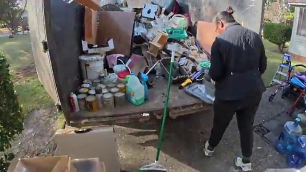 Household belongings and paint cans sorted on a trailer bed while a crew member works through the load