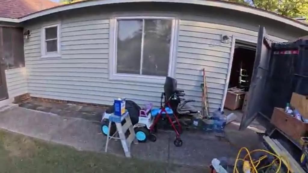 Household items, mobility equipment and stored clutter gathered along the side of an older single-story home