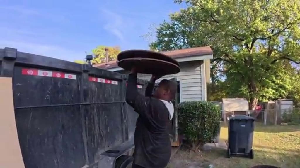 Hauler lifting a discarded table top into a dump trailer during a furniture pickup